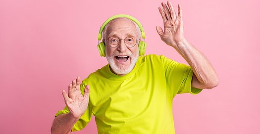 Ein älterer Mann im gelben T-Shirt tanzt zur Musik auf seinen Kopfhörern